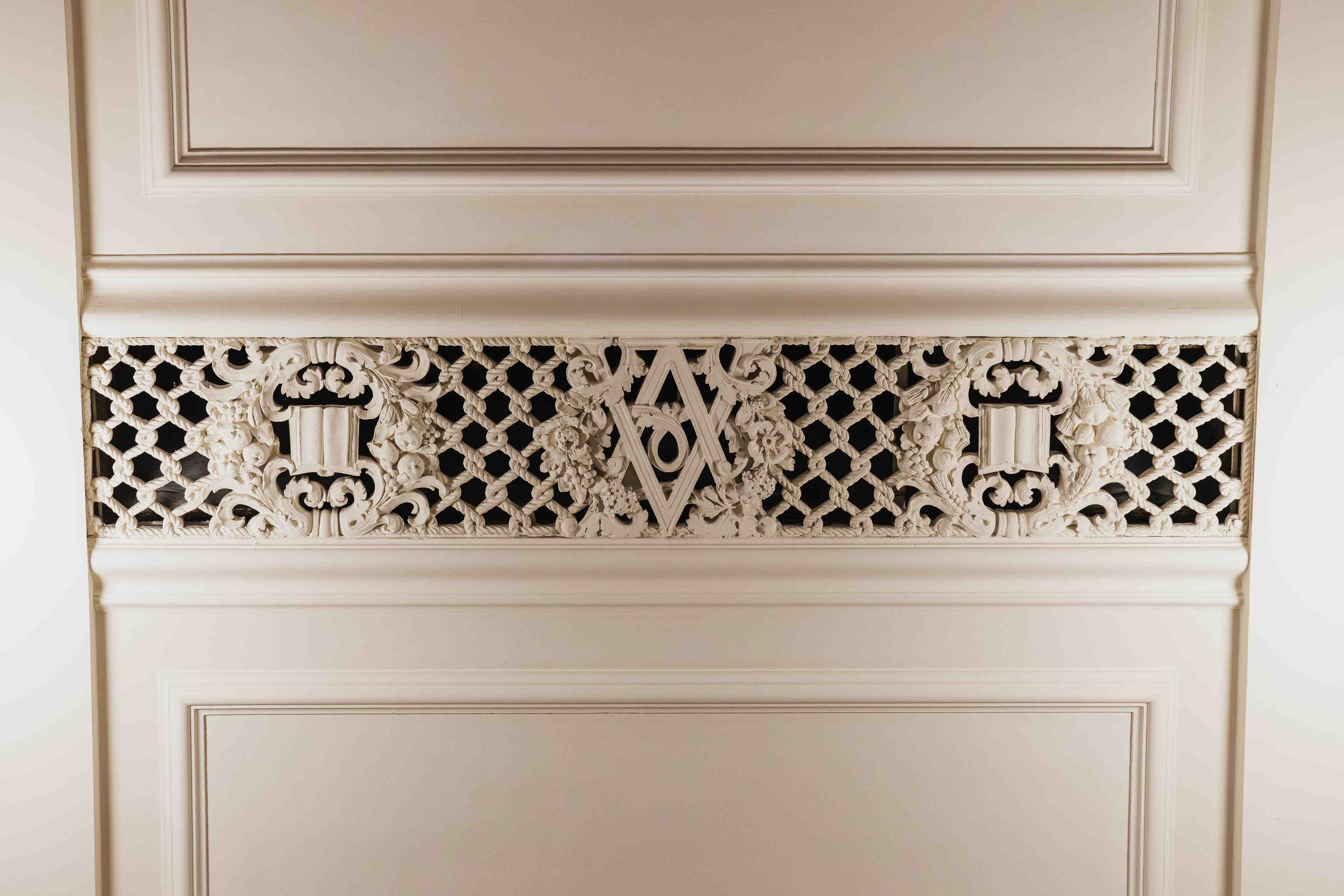 Ornate cream-colored carved wall panel featuring decorative latticework, floral motifs, scrollwork, and a central geometric emblem.